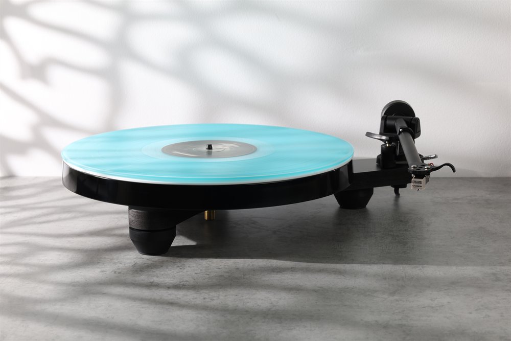 La Rega Replay en noir mat à la maison sur une surface en pierre, un disque turquoise sur le plateau, des ombres de feuilles au mur.
