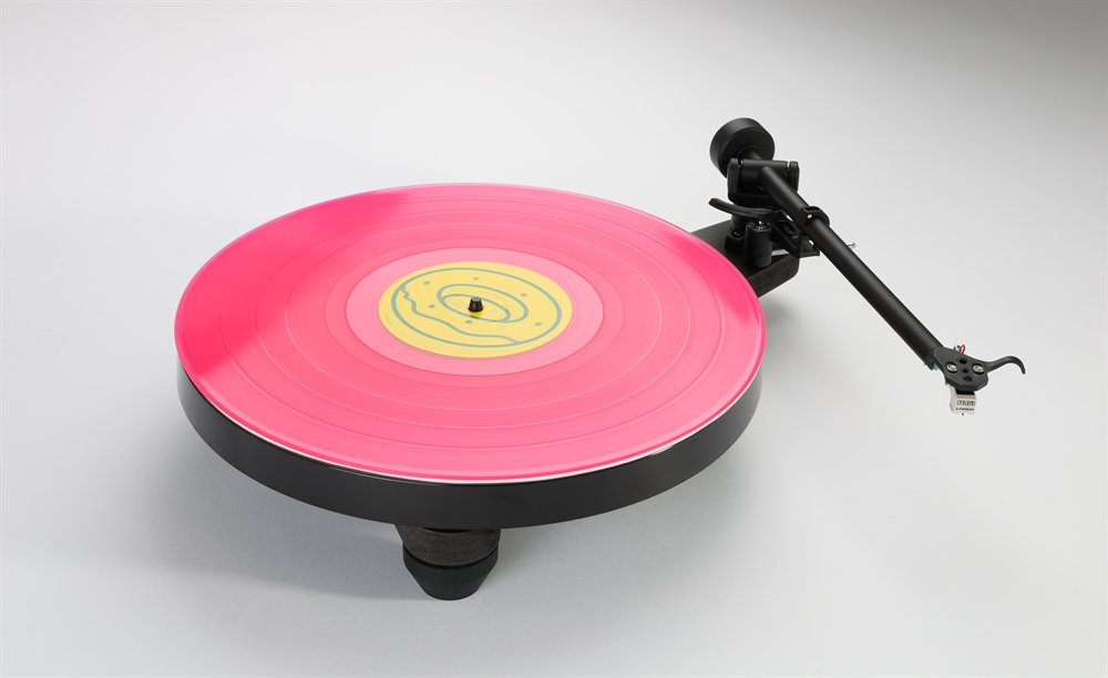 La Rega Replay en noir mat, vue de trois quarts par le dessus, un disque rose sur le plateau et le bras RB110 sur son repose-bras.
